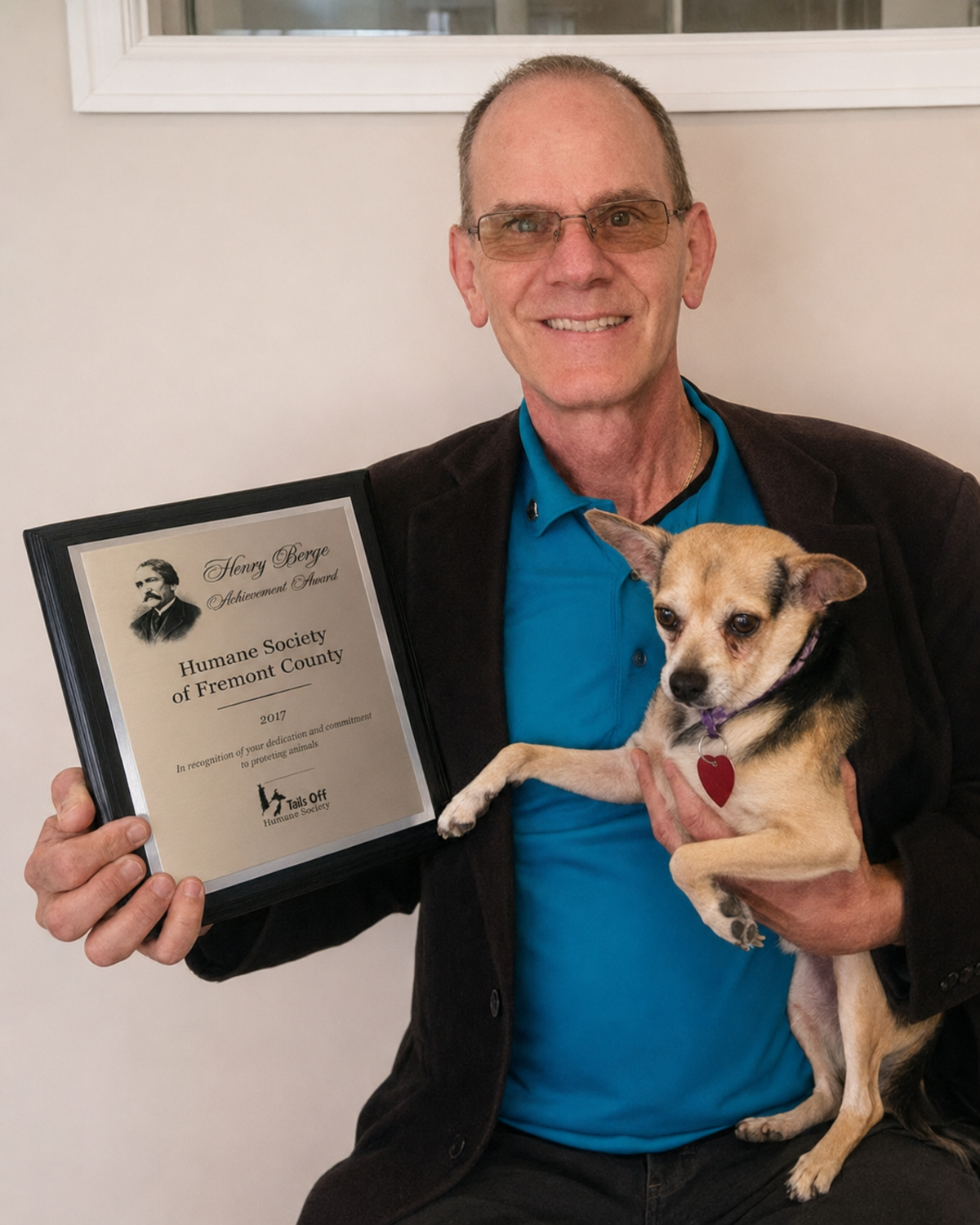 Shelter leader Doug Rae holding a small dog and a humane service award